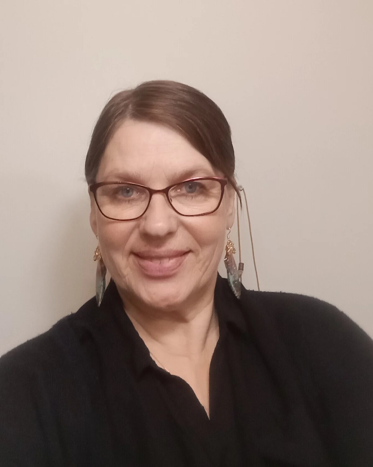 Seija Tauriainen, taideterapiaohjaaja, hymyilee mustassa paidassa vaaleaa taustaa vasten.